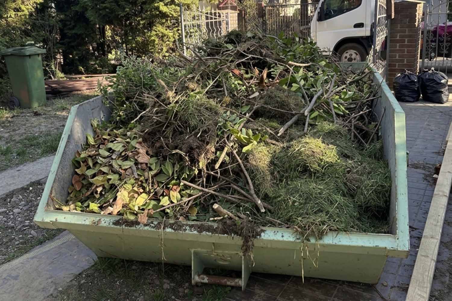 Kontener wypełniony gałęziami, krzewami i liśćmi z porządków w ogrodzie