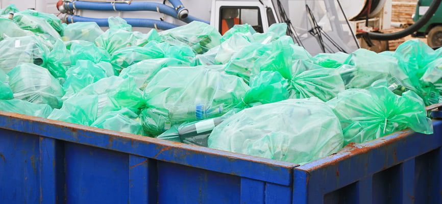 Niebieski kontener wypełniony zielonymi workami z odpadami